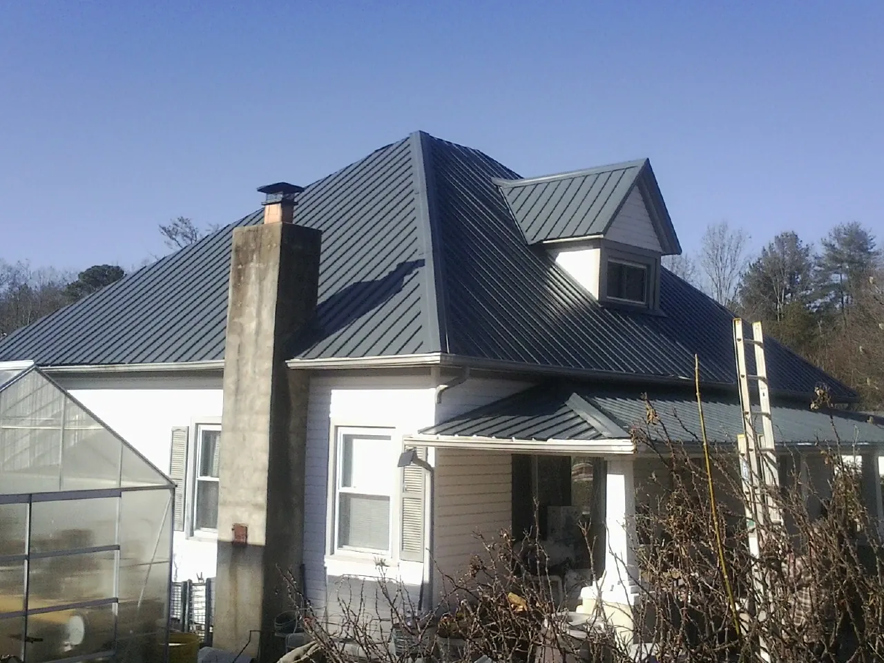 Dark blue standing seam metal roof on a white farmhouse with dormer — Slate & Tile Roof Repair by Roofing Brothers in Emington