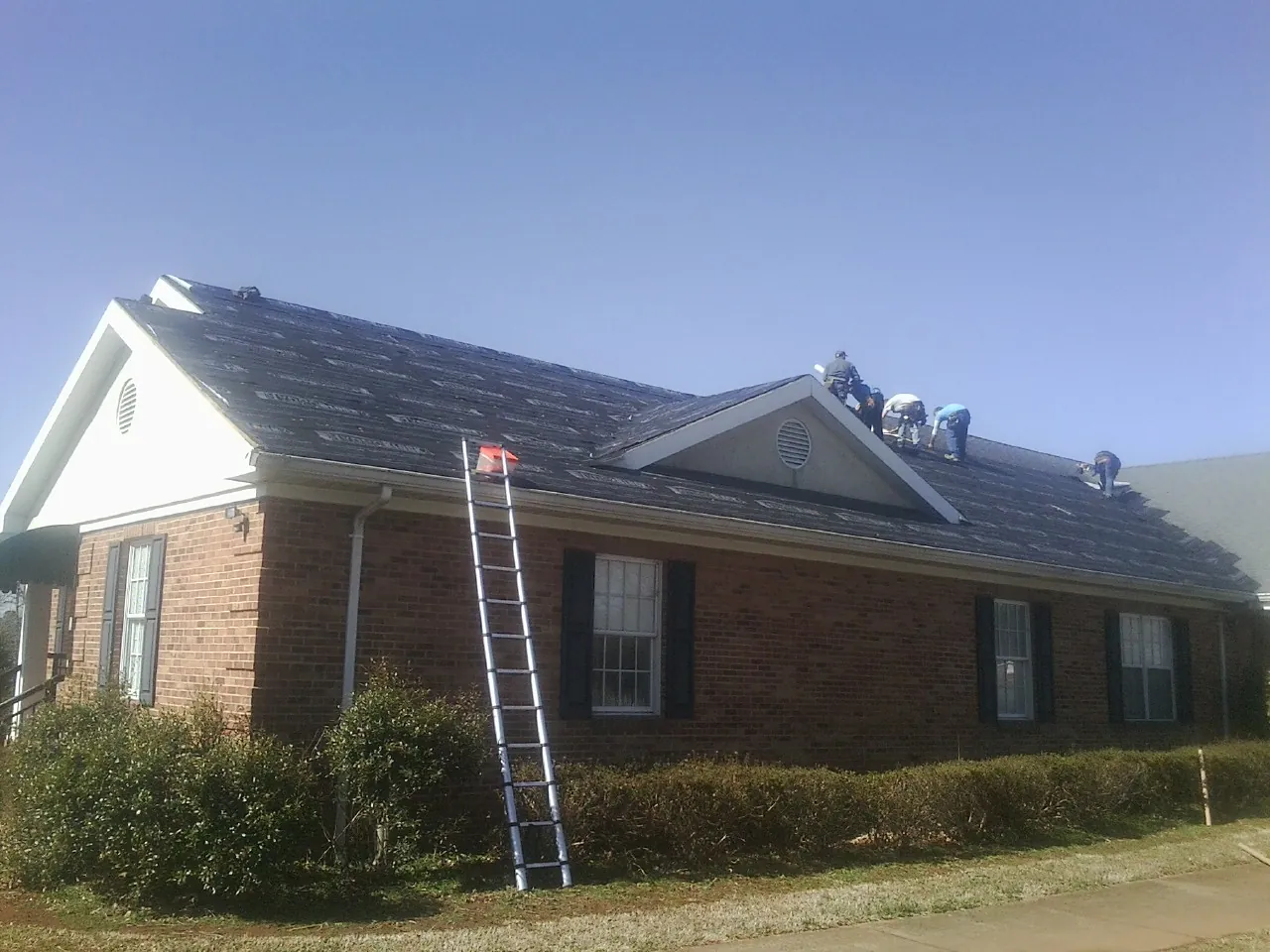Crew tearing shingles off a brick ranch roof with a ladder set — Emergency Roof Repair work by our crew in Emington