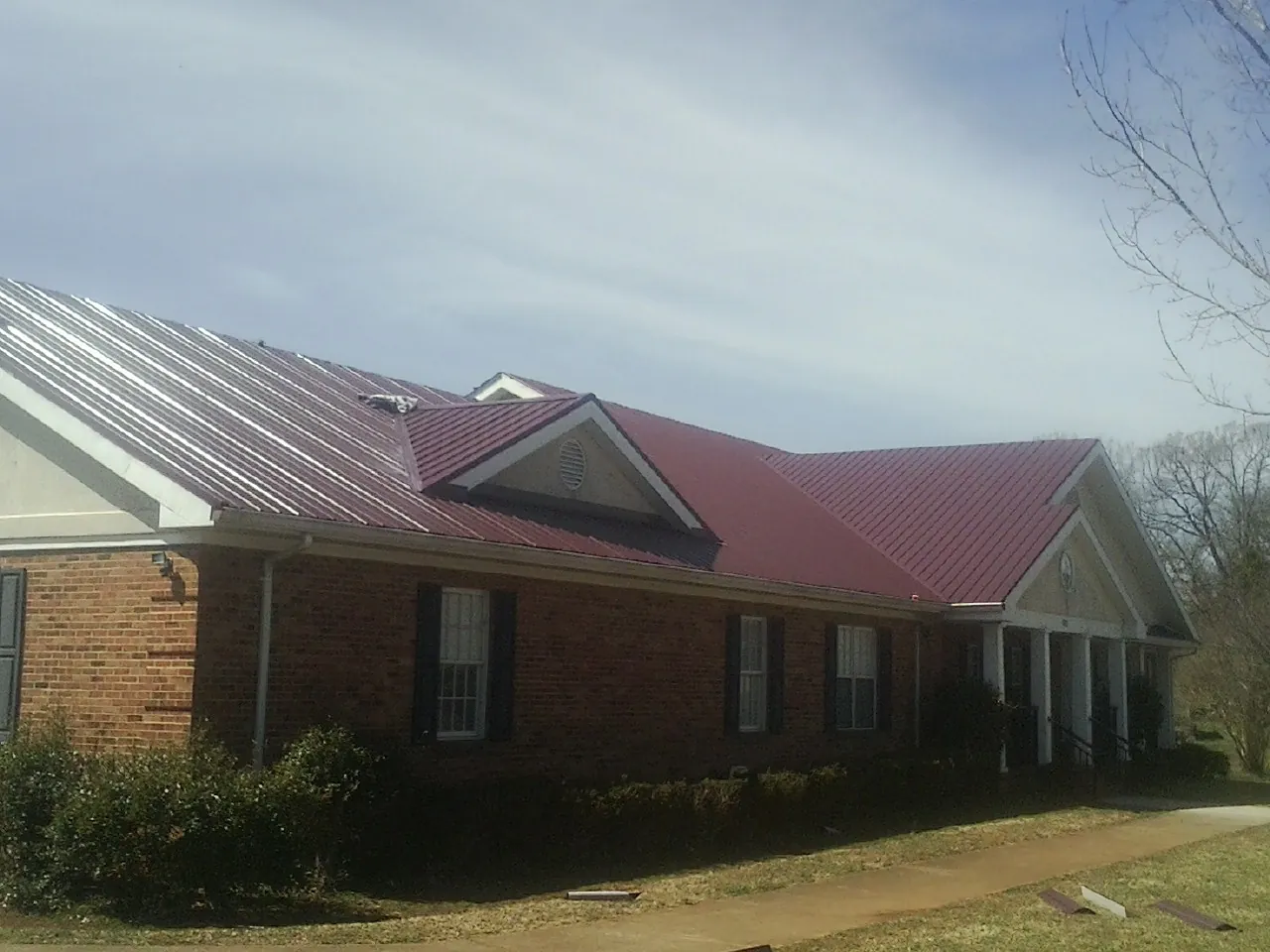 Red metal roof with gabled entries on a long brick building, from a Hail Damage Roof Repair job in Emington