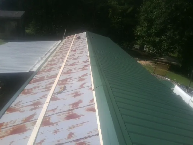 Old rusted panels beside newly installed green metal roofing — Wind Damage Roof Repair by Roofing Brothers in Emington