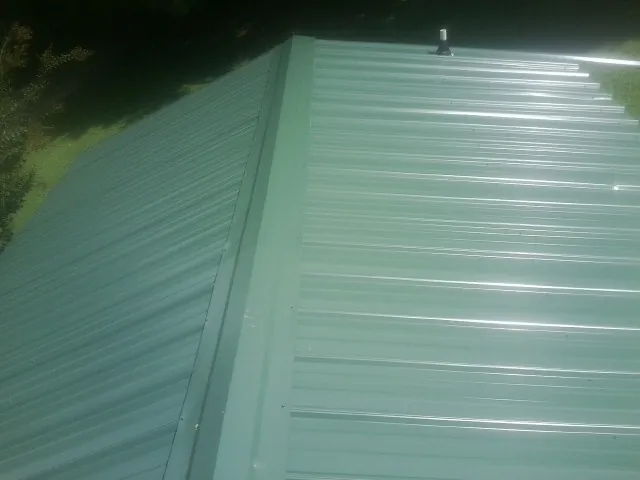 New green metal panels meeting at the ridge of a roof — Flat Roof Repair work by our crew in Emington
