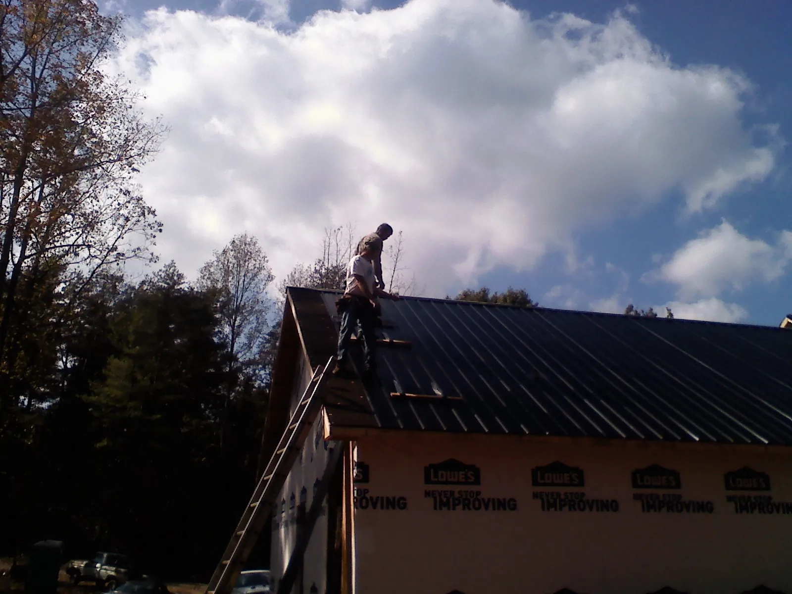 Roofer fastening dark metal panels high against a cloudy sky, from a Roof Inspection job in Emington