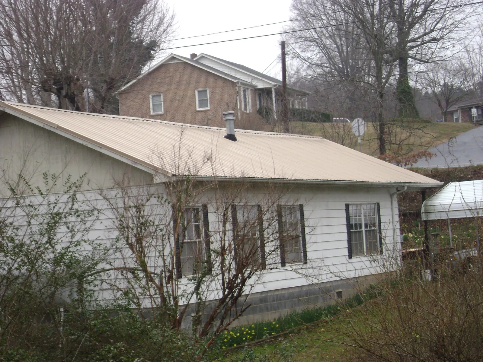Tan metal roof on a white sided house set into a hillside — Commercial Roofing by Roofing Brothers in Emington